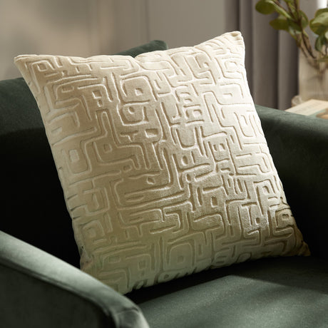 Soren Abstract Velvet Cushion in Chalk, a square cut-velvet cushion with a raised geometric pattern, shown on a dark green sofa in a living room setting.
