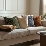 Soren Abstract Velvet Cushion in Chalk with a raised geometric pattern, shown centre on a beige sofa alongside green, grey, and rust cushions.