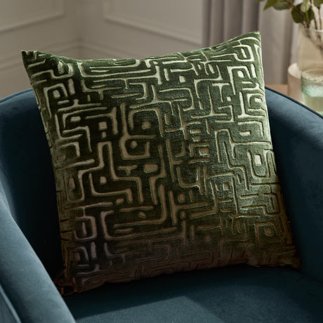 Soren Abstract Velvet Cushion in smoke green, 45cm square with a cut-velvet maze-like geometric pattern, shown on a dark blue armchair.