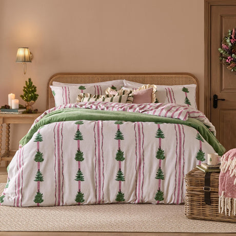 Spruce Stripes Cotton Reversible Duvet Cover Set in Oat with green pine trees between pink and green stripes, styled with green throw and cushions on a bed with rattan headboard.