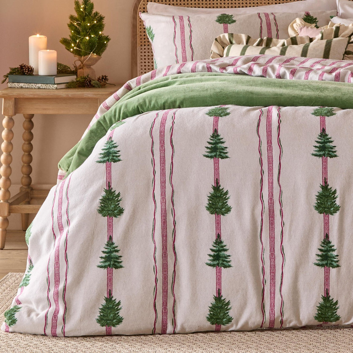 Spruce Stripes Cotton Reversible Duvet Cover Set in oat, shown on a bed with green tree stripe design, pink pinstripes, and green throw, styled in a bedroom with a wooden nightstand and candles.