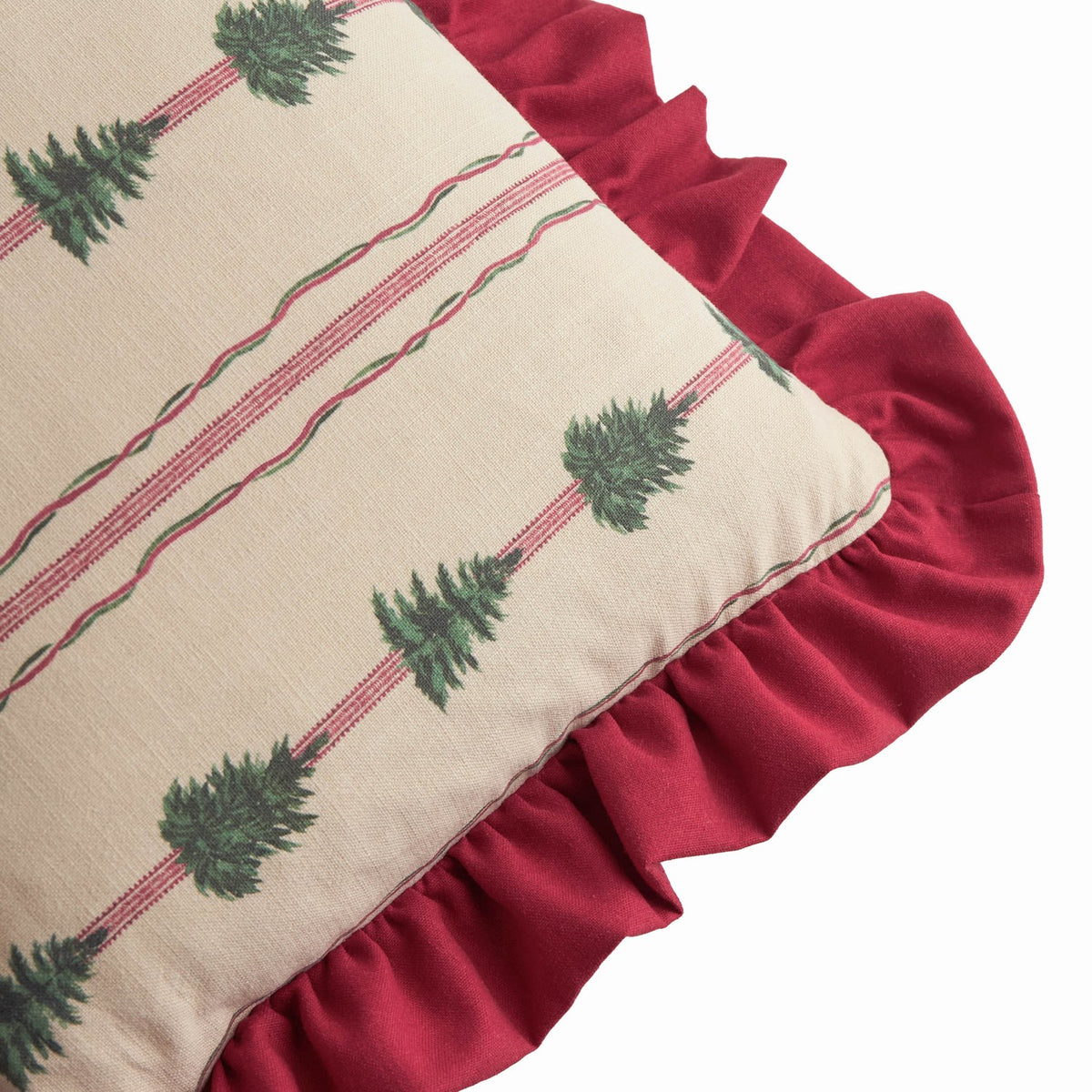 Spruce Stripes linen-cotton cushion corner detail showing beige fabric with green fir tree print, red and green stripes, and a gathered dark red ruffle edge.