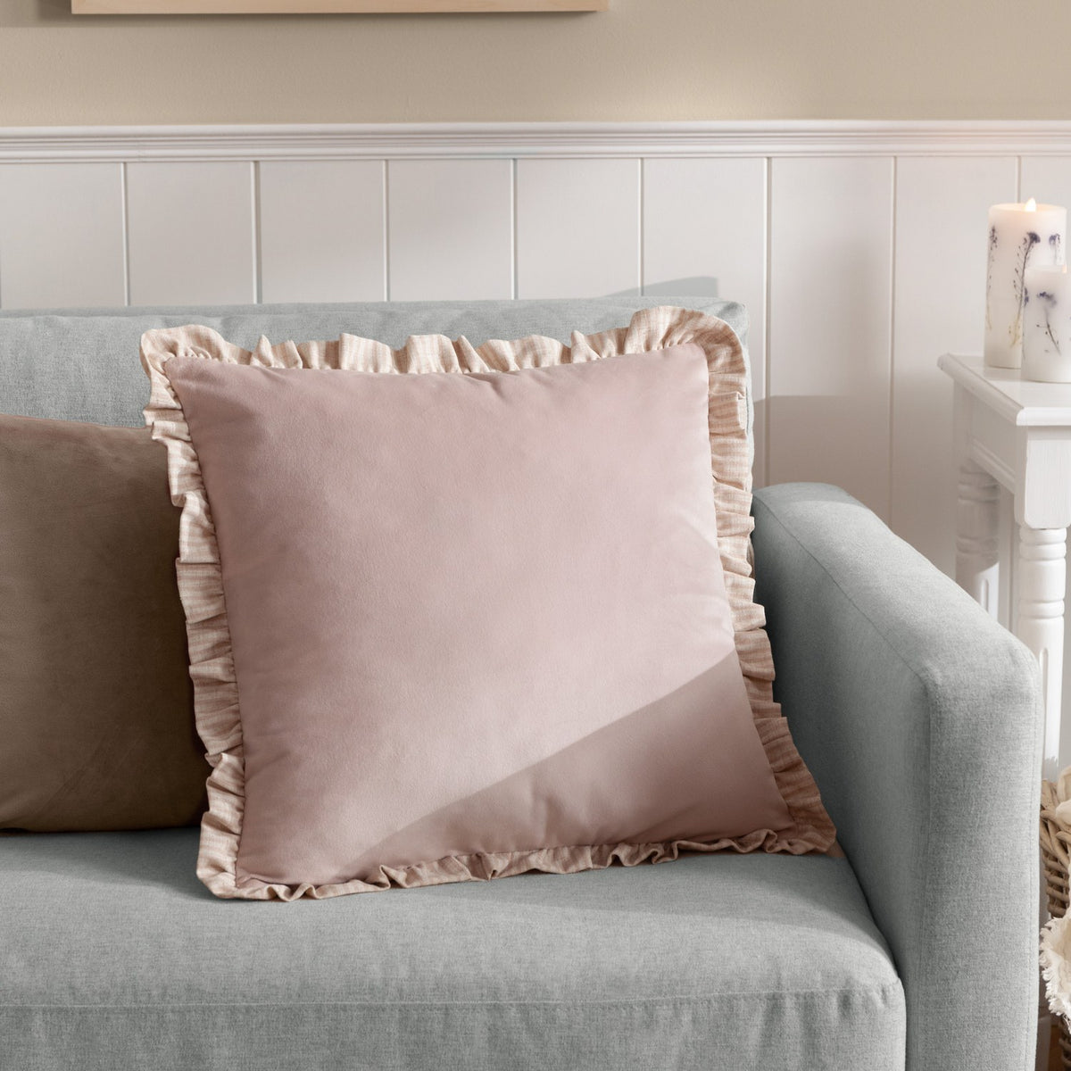 Solene Ruffle Velvet Linen Cushion in blush pink, square with matt velvet face and gathered linen-stripe ruffle trim, shown on a grey sofa.