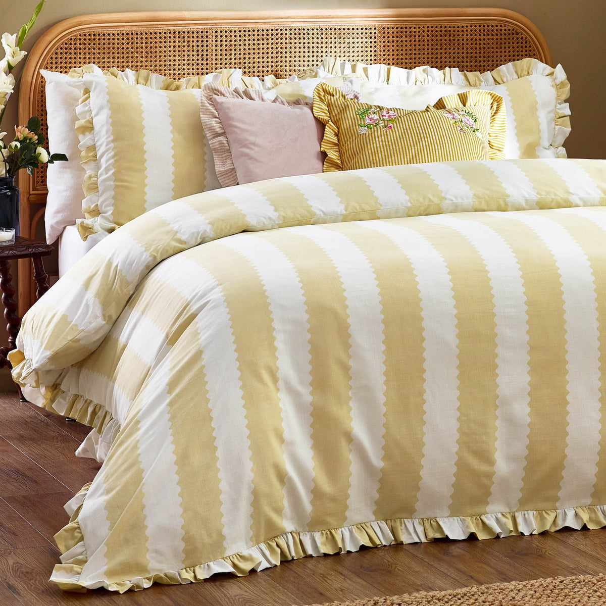 Solene Ruffle Velvet Linen Cushion in pink on a striped yellow and white bed, square velvet cushion with gathered ruffle trim, styled among patterned pillows.