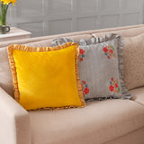 Solene Ruffle Velvet Linen Cushion in yellow with striped ruffle trim, shown on a beige sofa alongside a striped floral cushion in a living room setting.