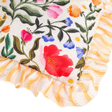 Close-up of the Summer Solstice reversible polyester cushion showing a cream floral corner with pink, red and blue blooms, edged in a yellow wavy-stripe ruffled trim.