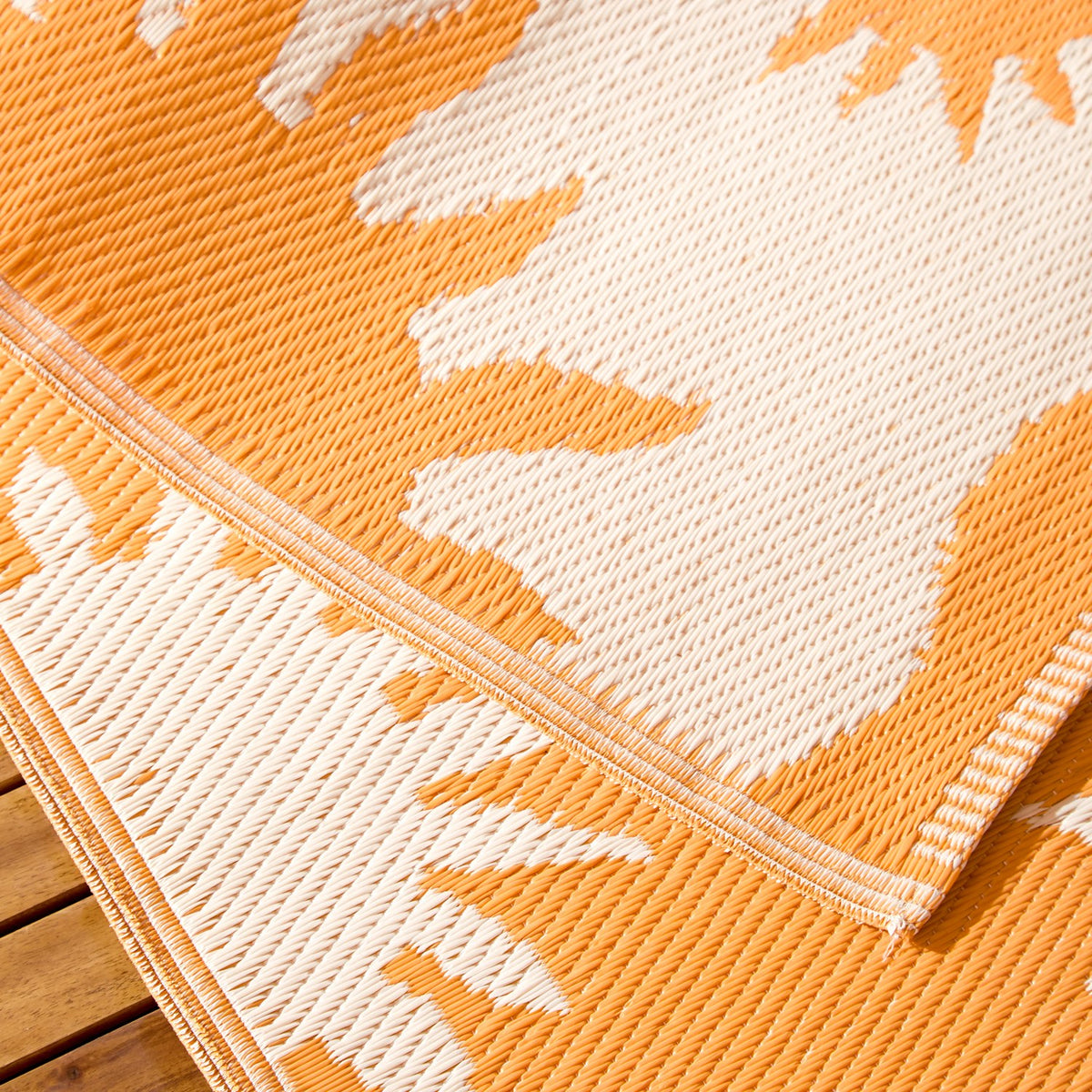 Close-up of the Summer Solstice Reversible Abstract Rug in Sunrise Yellow, showing woven polypropylene texture, orange and cream sun motif, and a folded edge revealing the reverse side.