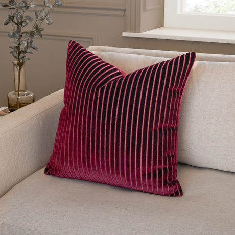 Savoy Stripe Polyester Velvet Cushion in burgundy with ribbed vertical stripes and metallic thread detail, shown on a beige sofa in a living room setting.
