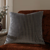 Savoy Stripe square cushion in charcoal grey velvet with cut-pile stripes and fine metallic threads, shown on a rust velvet sofa in a living room setting.