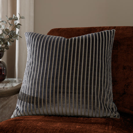 Savoy Stripe square cushion in charcoal grey velvet with cut-pile stripes and fine metallic threads, shown on a rust velvet sofa in a living room setting.
