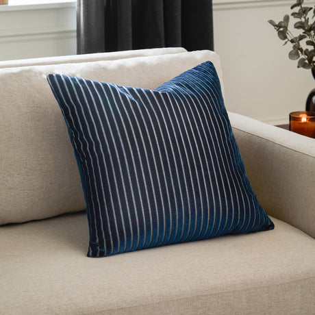 Savoy Stripe Polyester Velvet Cushion in navy with fine vertical stripes on a cut velvet front, shown on a cream sofa in a living room setting.