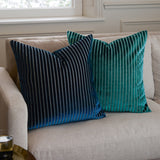 Savoy Stripe velvet cushion in navy with fine vertical striped front, shown 50x50cm square on a beige sofa beside a matching teal striped cushion.