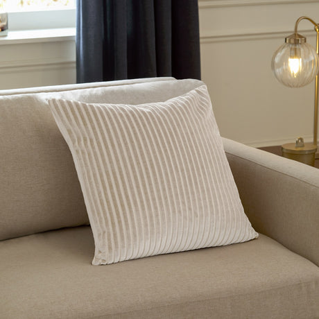 Savoy Stripe Polyester Velvet Cushion in Oyster, a square cut-velvet cushion with vertical ribbed texture, shown propped on a beige sofa in a living room setting.