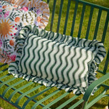 Summer Solstice Wiggly Stripe rectangular outdoor cushion in green wavy stripes with off-white ground and ruffled edge, shown on a green garden bench.