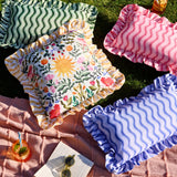 Green wiggly stripe rectangular cushion with ruffled edge, shown outdoors on grass alongside pink and blue striped cushions and a floral print cushion.