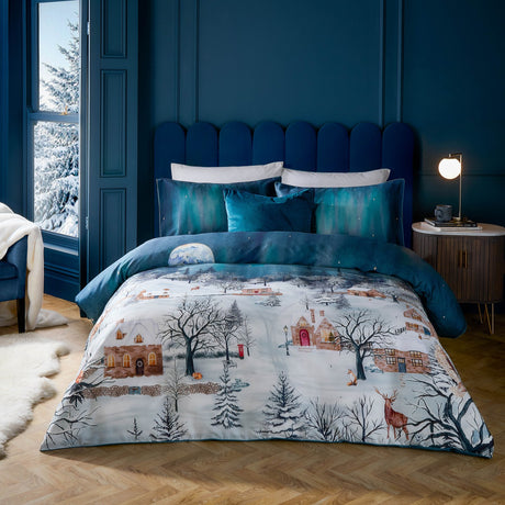 Starlight Cotton Piped Duvet Cover Set in midnight blue on a bed in a navy bedroom, showing a printed snowy village scene with cottages, trees, a stag and fox, paired with teal cushions.