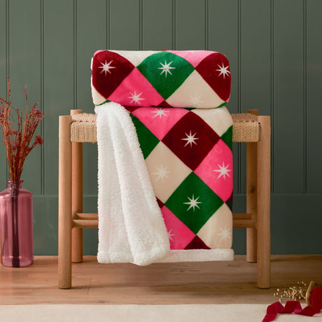 Star Sherpa Geometric Polyester Throw in multicoloured diamond print with white star motifs, cream sherpa reverse, draped over a wooden stool in a living room setting.