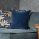 Stitch Plain Velvet Cushion in deep bluebell blue with contrasting ecru blanket stitch edging, shown on a teal velvet sofa beside a patterned cushion.