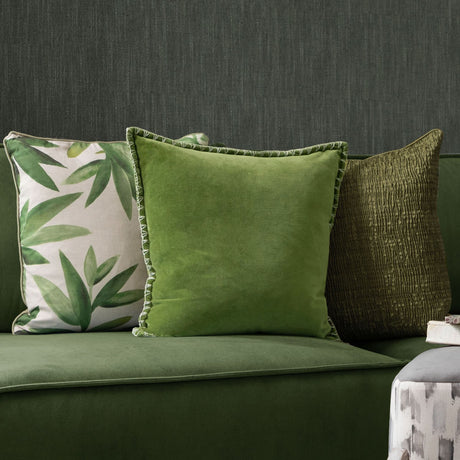 Stitch Plain Velvet Cushion in grass green with pale contrast blanket-stitch edging, shown on a green sofa beside patterned and textured cushions.