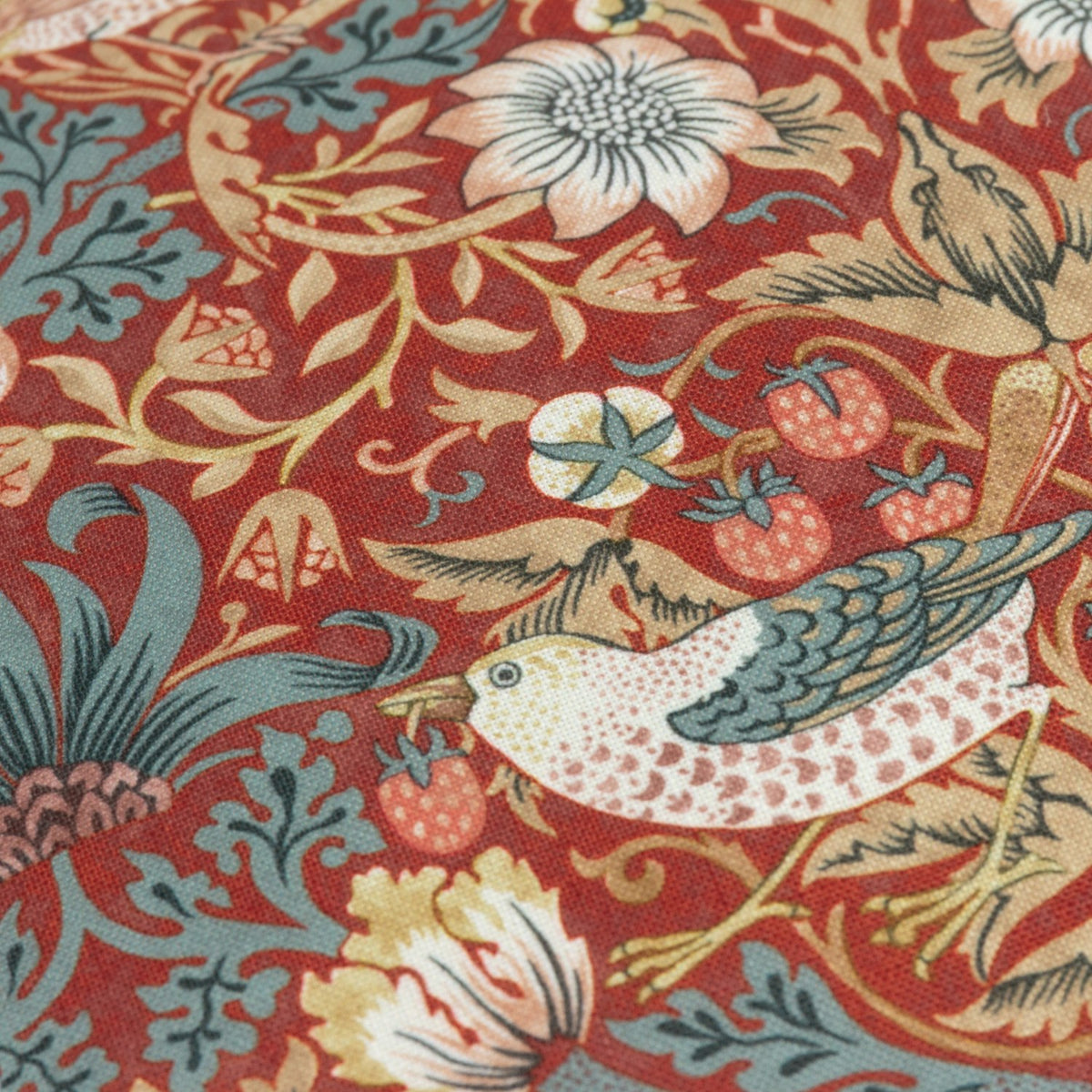 Close-up of the Strawberry Thief Floral Polyester Cushion in Berry, showing a bird, strawberries and floral trails in blue, cream and gold on a deep red ground.