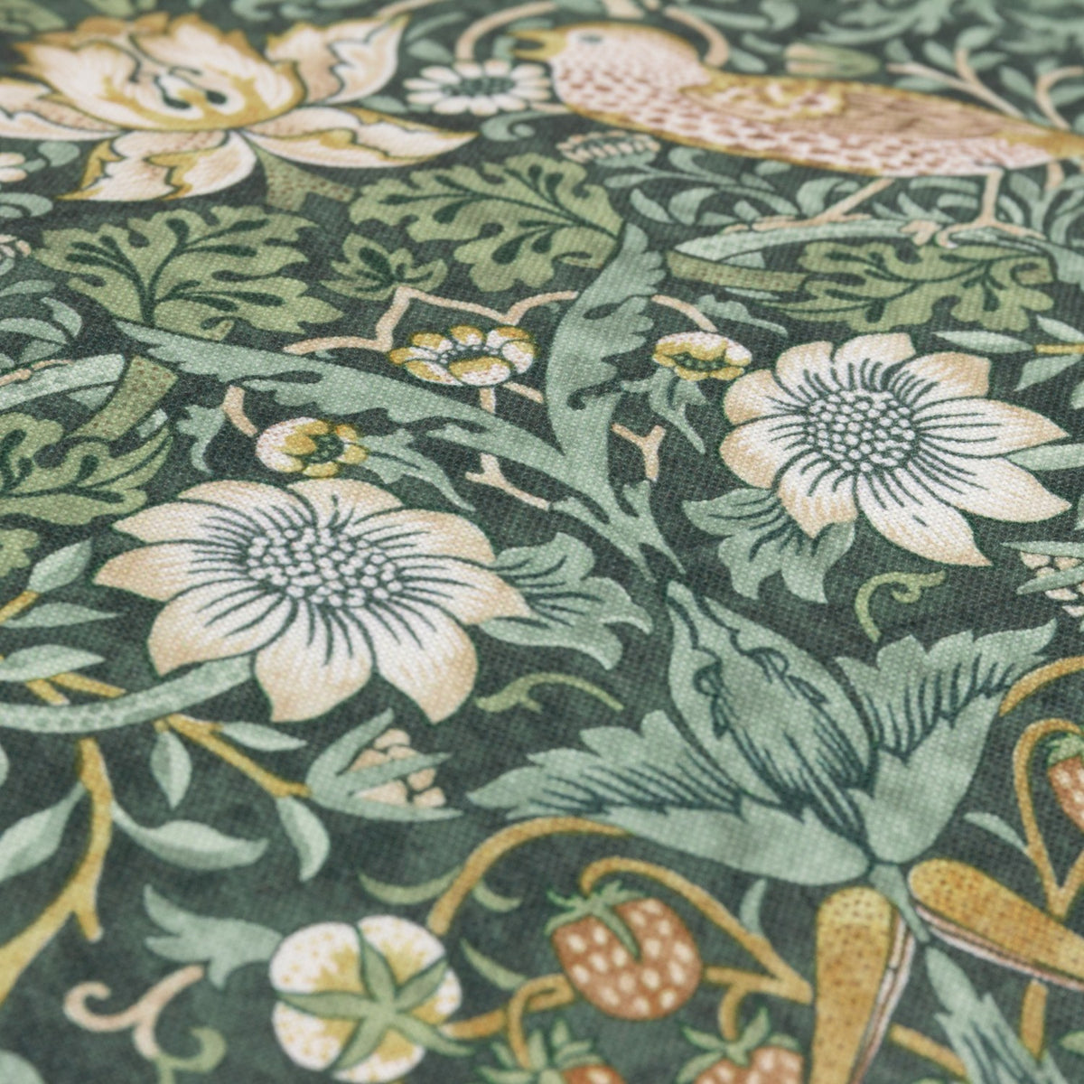 Close-up of the Strawberry Thief Floral polyester cushion in Forest Green, showing bird, strawberry and floral motifs printed in cream, tan and green on a deep green ground.