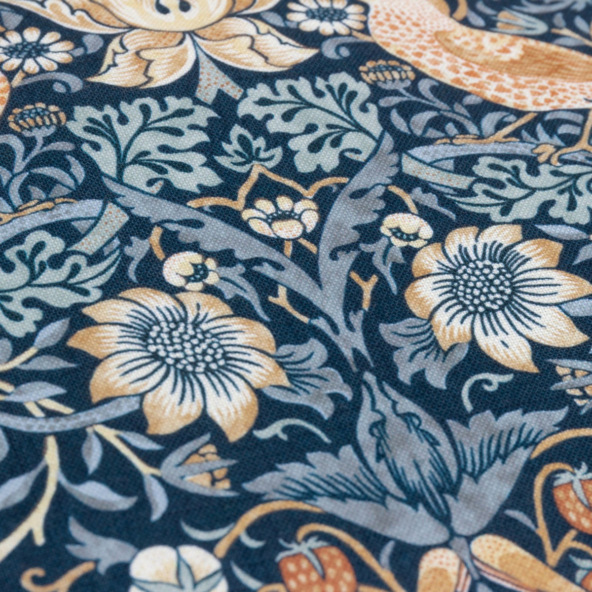 Close-up of the Strawberry Thief Floral Polyester Cushion in indigo, showing William Morris's dense pattern of birds, strawberries and flowers in amber, cream and pale blue on a deep indigo ground.