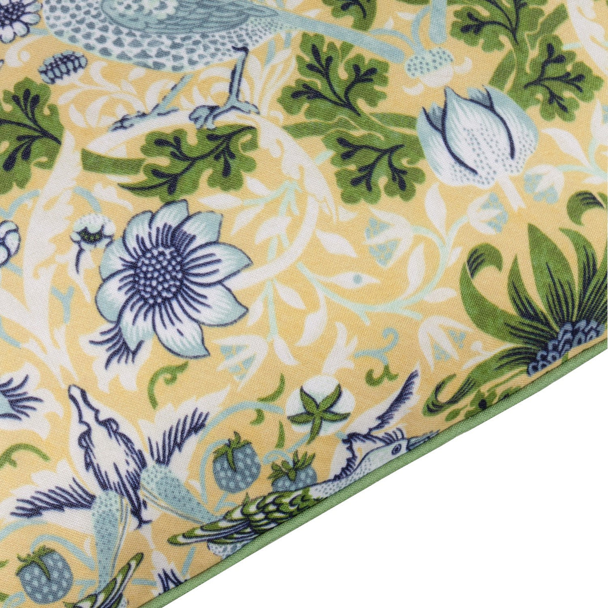 Corner detail of the Strawberry Thief Floral Polyester Cushion in Sunflower, showing thrushes, berries, and indigo-blue flowers on yellow fabric with green piping edge.