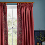 Berry red velvet pencil pleat curtains with Strawberry Thief embroidered leading edge, shown hanging beside a window on a wooden pole in a blue-walled room.