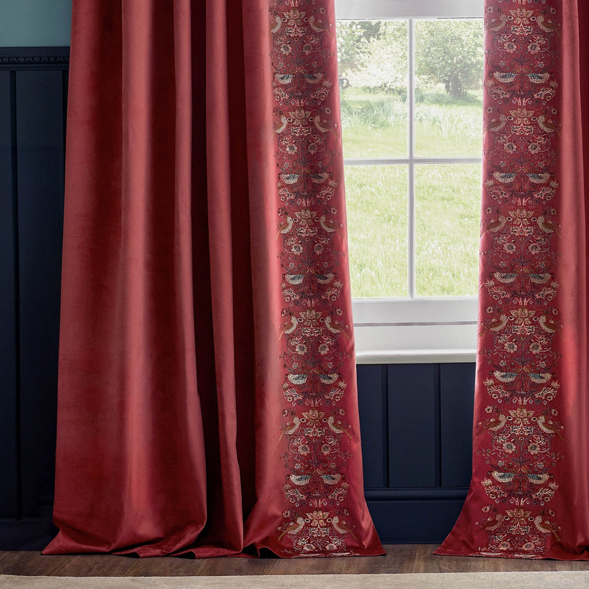 Berry red velvet pencil pleat curtains with Strawberry Thief embroidered leading edge in birds and foliage, shown framing a window in a room with navy panelling.