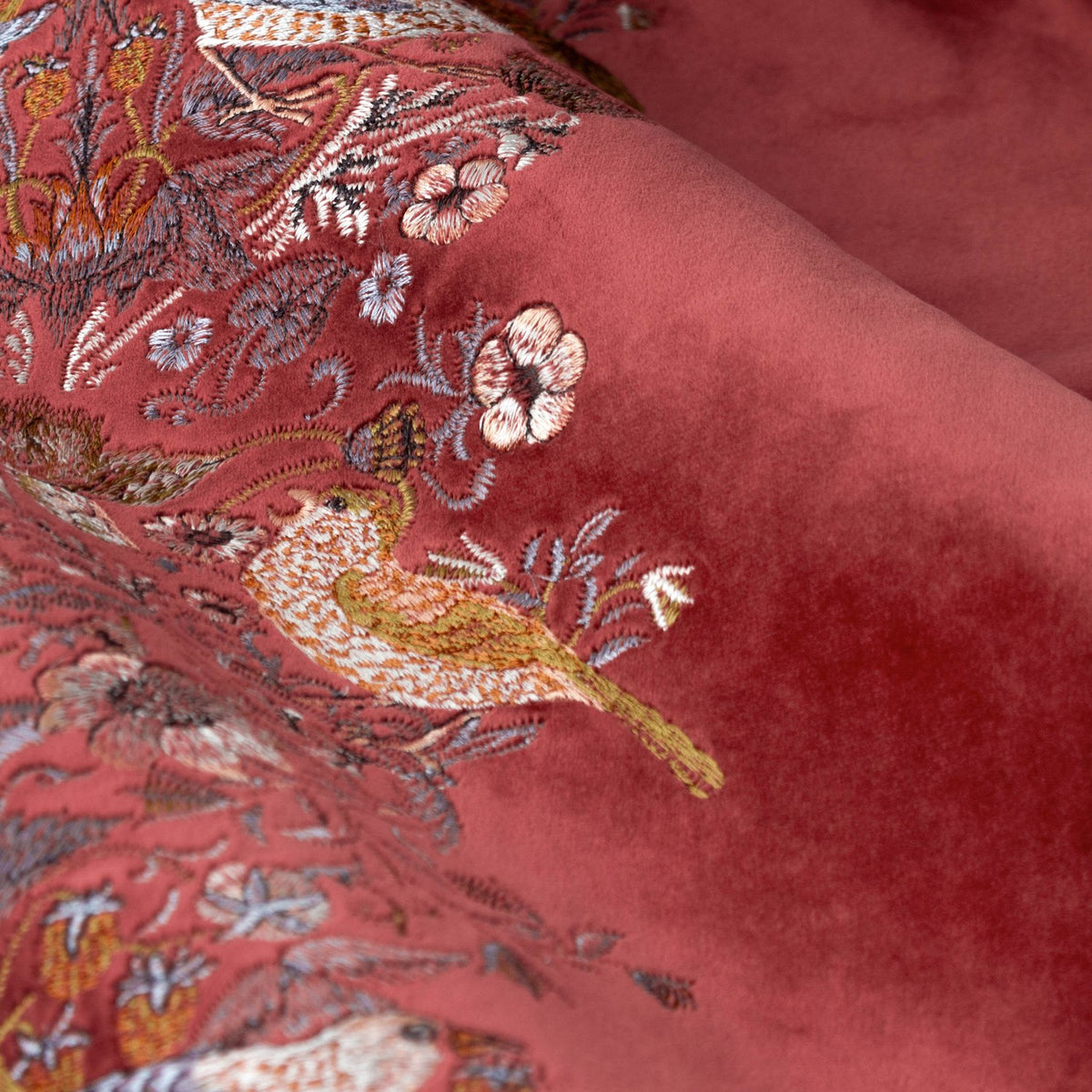 Close-up of Strawberry Thief pencil pleat curtains in berry red velvet, showing an embroidered leading edge with birds, strawberries and scrolling foliage.