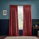 Berry red velvet pencil pleat curtains with embroidered Strawberry Thief bird and foliage band on the inner edge, hung on a wooden pole in a blue-panelled room.