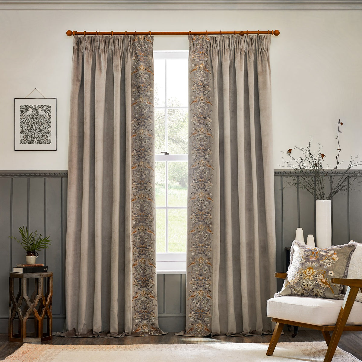 Biscuit velvet pencil pleat curtains with embroidered Strawberry Thief leading edge, hung on a wooden pole in a living room with panelled walls.