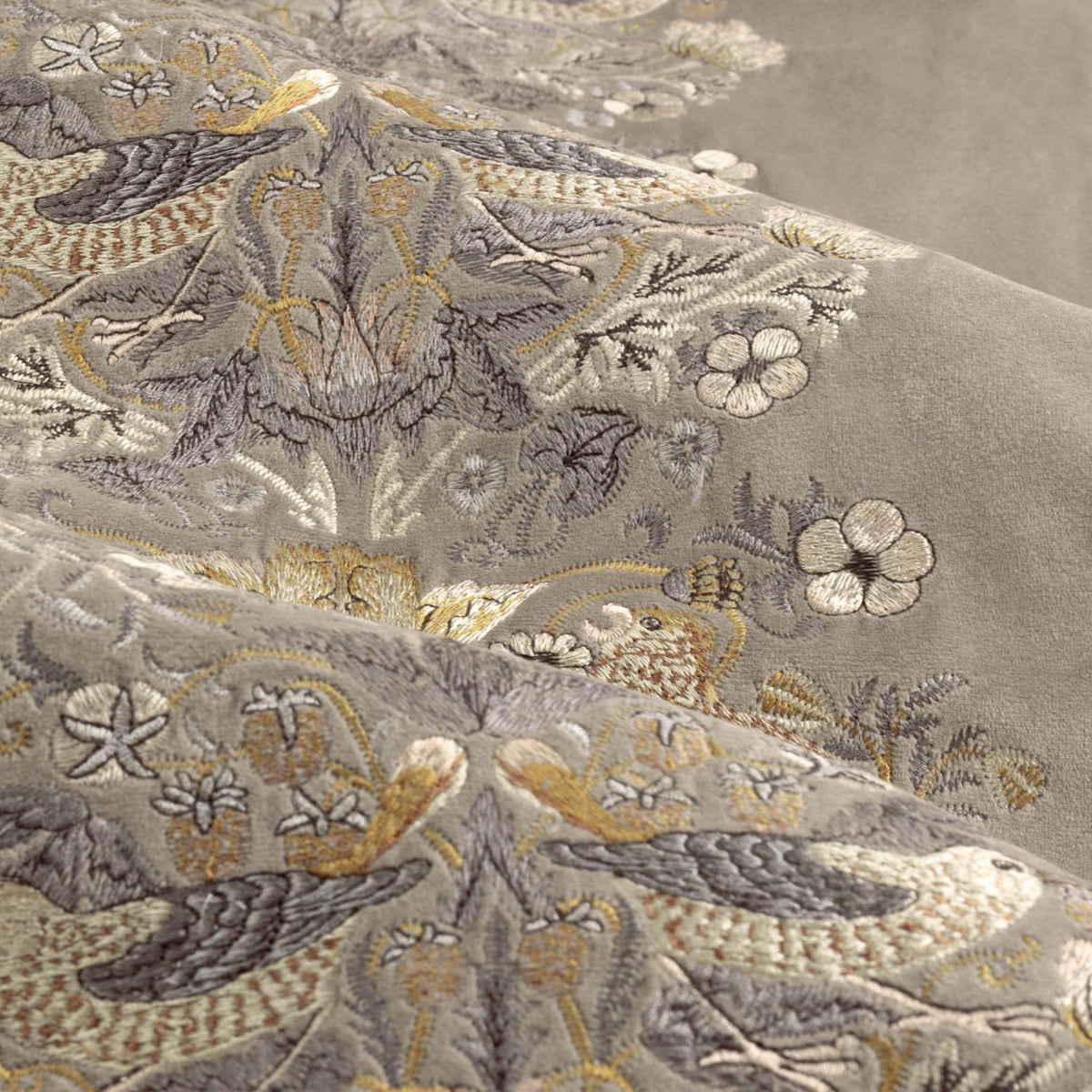 Close-up of biscuit velvet pencil pleat curtain fabric with embroidered Strawberry Thief design featuring birds and flowers in grey, gold and cream tones.