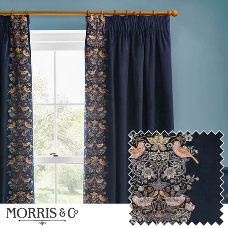 Indigo velvet pencil pleat curtains with Strawberry Thief bird and floral embroidery down the leading edge, shown pleated on a wooden pole beside a window in a blue-walled room.