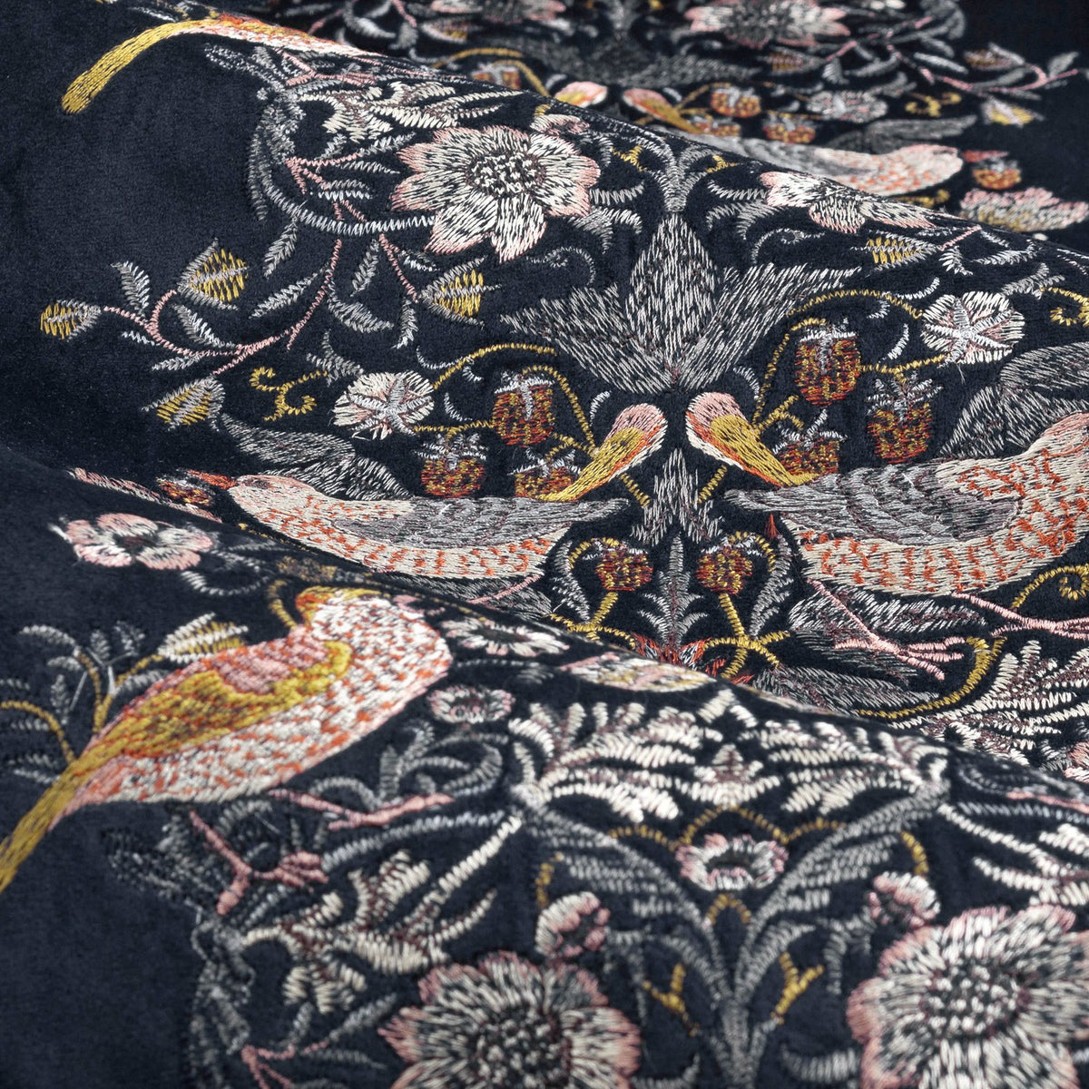 Close-up of Strawberry Thief pencil pleat curtain fabric in indigo velvet, showing embroidered thrush birds and florals in rust, gold, sage and cream thread.