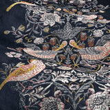 Close-up of Strawberry Thief pencil pleat curtain fabric in indigo velvet, showing embroidered thrush birds and florals in rust, gold, sage and cream thread.