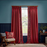 Strawberry Thief Jacquard Velvet Cushion in berry red on a bedroom armchair, with bird and floral embroidery, styled against red curtains and navy panelled walls.