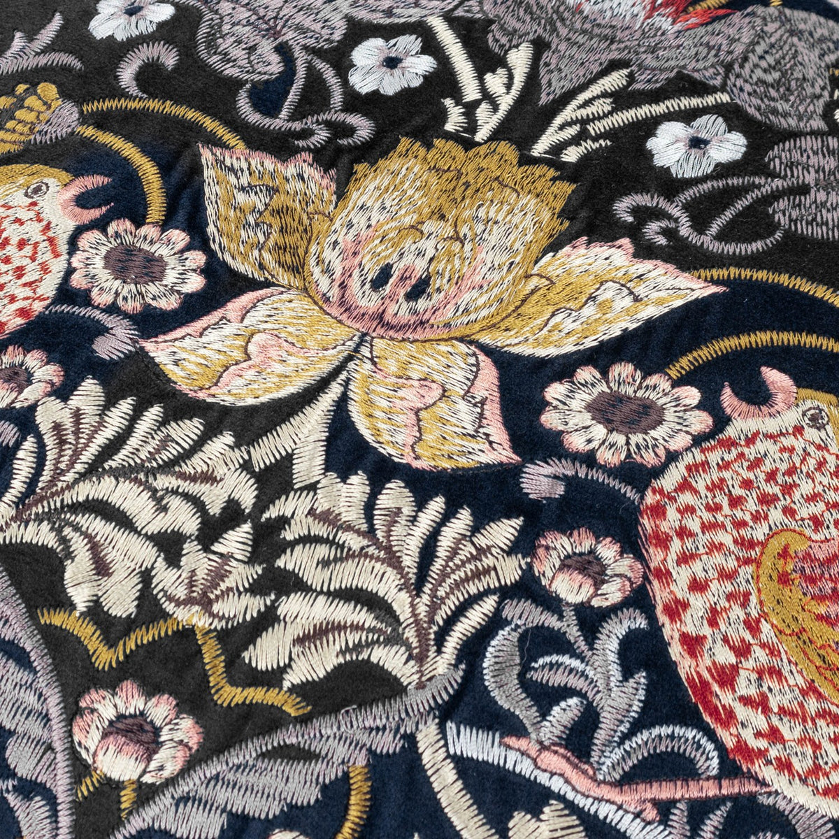 Close-up of the Strawberry Thief Jacquard Velvet Cushion in indigo, showing embroidered birds, strawberries and a golden central bloom on deep blue velvet with cream, gold, rust and pink detailing.