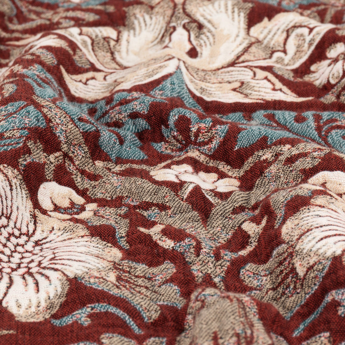 Close-up of the Strawberry Thief Jacquard Cotton Throw in Berry, showing woven birds and florals in cream, blue and brown on a deep red ground.