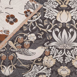 Strawberry Thief Jacquard Cotton Throw in biscuit, showing the folded corner reverse in cream with rust florals against the charcoal jacquard weave of birds, strawberries and flowers.