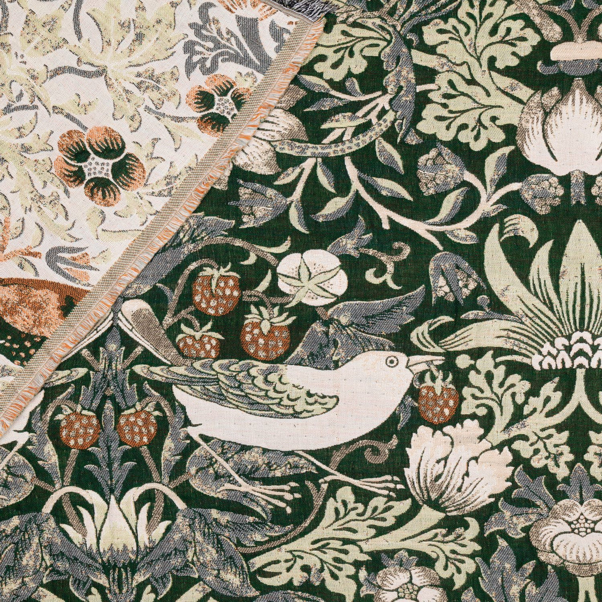 Strawberry Thief Jacquard Cotton Throw in forest green, folded corner showing cream reverse, with woven bird, strawberry, and foliage pattern.