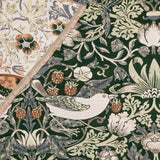 Strawberry Thief Jacquard Cotton Throw in forest green, folded corner showing cream reverse, with woven bird, strawberry, and foliage pattern.