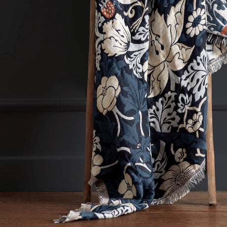 Strawberry Thief Jacquard Cotton Throw in indigo, draped over a wooden ladder, showing a fringed edge and woven floral pattern in cream, teal and rust tones.