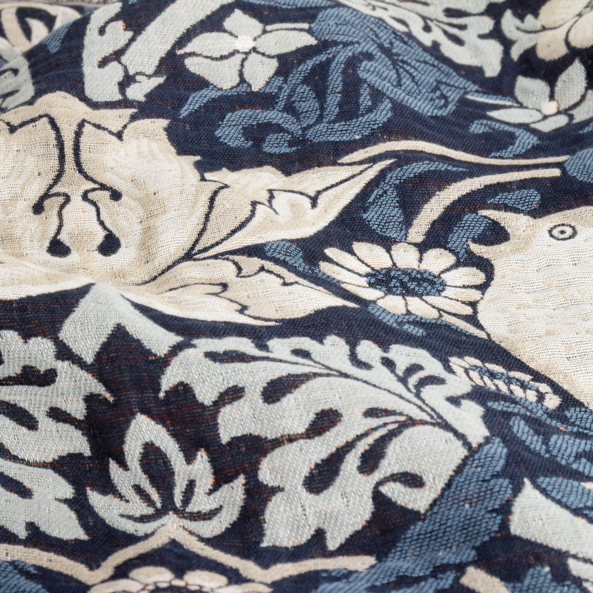 Close-up of the Strawberry Thief Jacquard Cotton Throw in indigo, showing woven bird, floral and berry motifs in cream and blue tones on a dark ground.
