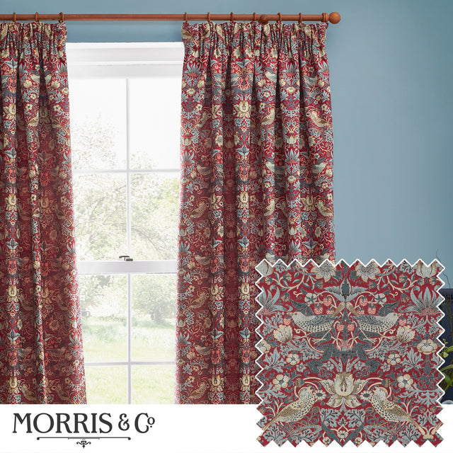 Strawberry Thief pencil pleat curtains in berry red jacquard fabric with bird and floral pattern, shown hanging from a wooden pole beside a window in a blue-walled room, with fabric swatch inset.