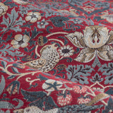 Close-up of Strawberry Thief pencil pleat curtain fabric in berry red, showing a jacquard-woven bird, floral, and strawberry motif in blue-grey and cream tones.