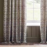 Pencil pleat curtains in Strawberry Thief jacquard, showing woven birds and foliage in grey, brown and biscuit tones, hung beside a window in a living room.