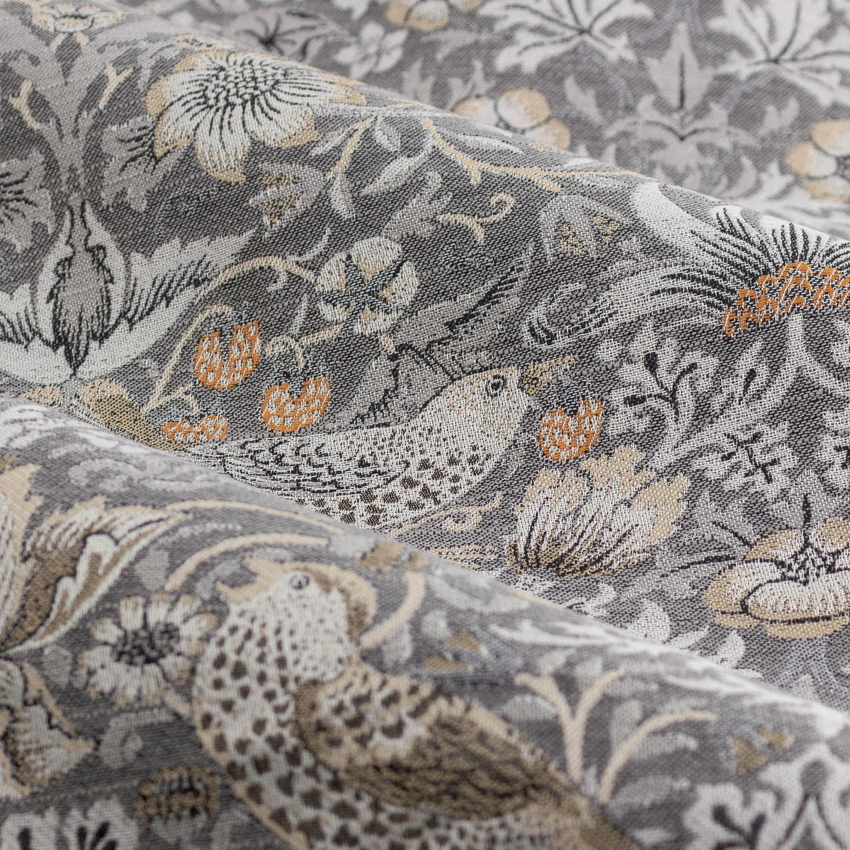 Close-up of Strawberry Thief pencil pleat curtain fabric in biscuit, a woven jacquard design of birds, strawberries and foliage in grey, cream and orange tones.