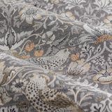 Close-up of Strawberry Thief pencil pleat curtain fabric in biscuit, a woven jacquard design of birds, strawberries and foliage in grey, cream and orange tones.