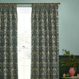 Strawberry Thief pencil pleat curtains in forest green polyester, featuring Morris & Co.'s bird and strawberry print, hung on a wooden pole beside a window in a duck-egg blue room.
